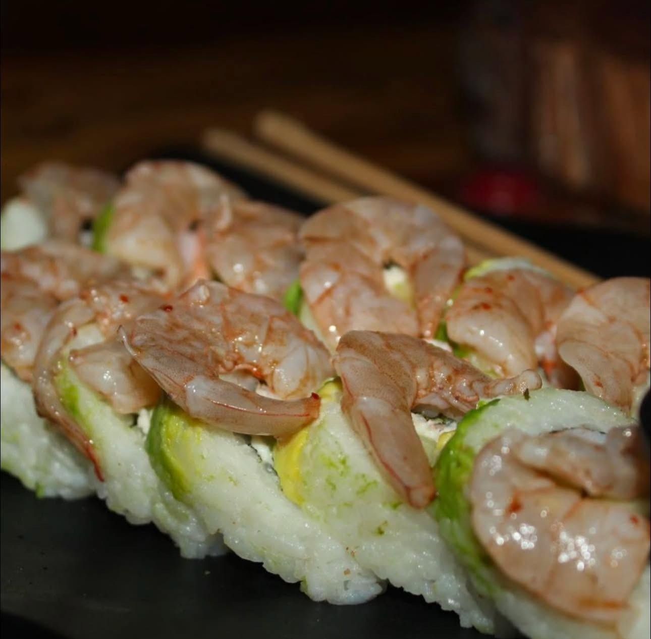 Rollo cubierto de aguacate con camarones encima, sobre plato negro